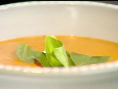 a white bowl filled with carrot soup and garnished with green leafy vegetables