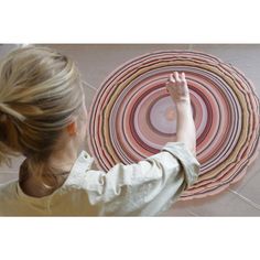 a woman standing in front of a circular rug on the floor with her hand up