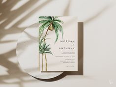 the palm tree wedding card is on top of a white plate with shadow from it