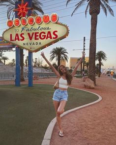 a woman posing in front of the famous las vegas sign at sunset with her arms up