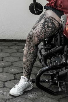 a man with tattoos on his legs sitting on a motorcycle