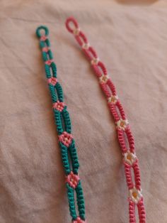 two necklaces are laying on top of a cloth covered tablecloth, one is green and the other is red