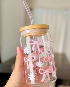 a person holding a mason jar with a straw in it and pink bows on the lid