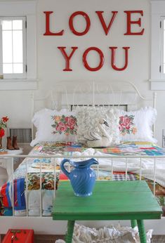 a white bed topped with a green table next to a red and white sign that says love you