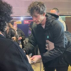 a man in black jacket standing next to a woman at a table with cell phone