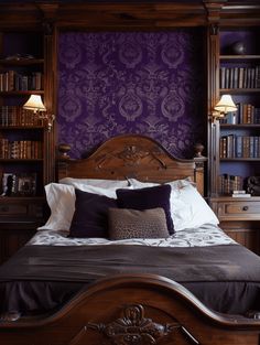 a bed with purple wallpaper and wooden headboard in front of bookshelves