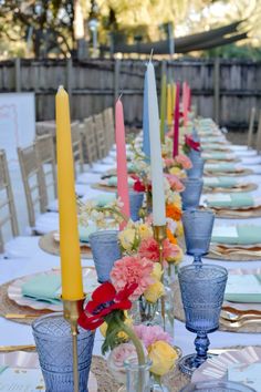 a long table is set with candles and flowers in blue glass vases on it