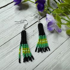 green, yellow and black seed beaded earrings on white wooden table next to purple flowers