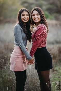 two young women standing next to each other in a field with tall grass and bushes