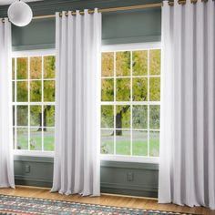 an open window with white curtains and a rug in front of it on top of a hard wood floor