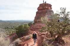 a man walking down a dirt path next to a tall red rock formation in the desert