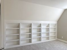 an empty room with white bookcases and carpeted flooring in the corner