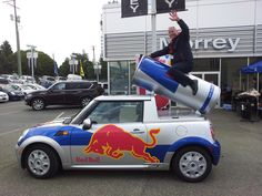 a man is sitting on top of a car with a red bull painted on it