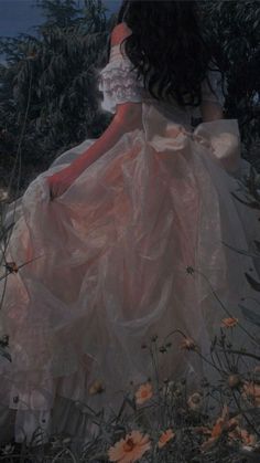 a woman in a white dress sitting on top of a lush green field next to flowers