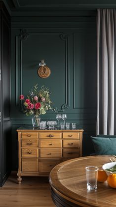 a dining room with green walls and wooden furniture, flowers in vases on the table