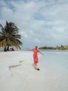 a woman standing on top of a sandy beach next to the ocean and palm trees