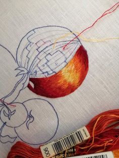 two skeins of thread next to an orange and red ball of yarn on a white tablecloth