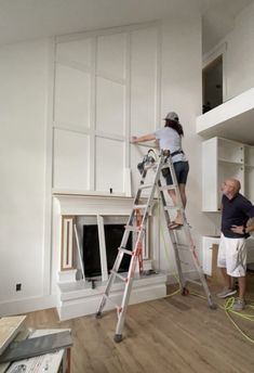 two people standing on ladders in front of a white wall with open shelves and cabinets