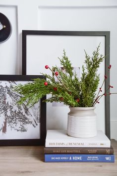 a white vase filled with greenery sitting on top of a table next to two books