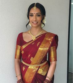 a woman in a red and gold sari with her hands on her hips posing for the camera