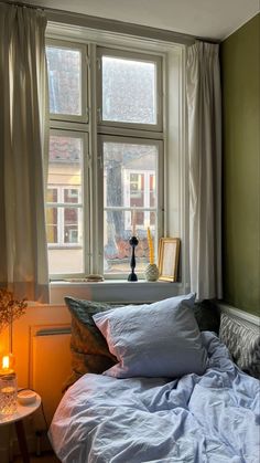 a bed sitting in front of a window next to a table with a lamp on it