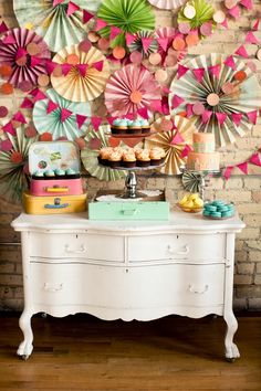 a table topped with lots of colorful paper fans next to a wall covered in cupcakes