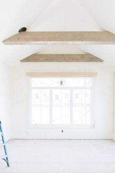 an empty room with white walls and a ladder in front of the window that is being painted