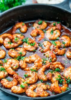 a skillet filled with cooked shrimp and garnished with parsley on the side