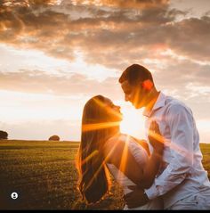 a man and woman are kissing in the field at sunset with the sun shining through the clouds