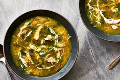 two bowls of soup with chicken and spinach on the side next to spoons