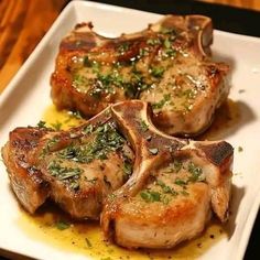 three pieces of meat sitting on top of a white plate covered in sauce and garnish