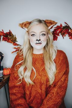 a woman with long blonde hair wearing a fake cat's nose and orange sweater