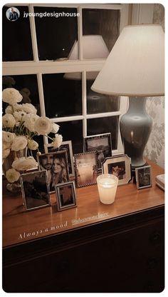 a table topped with pictures and a lamp next to a window covered in white flowers