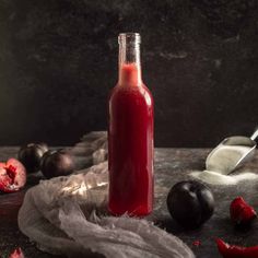 a bottle filled with red liquid next to some fruit