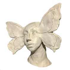 a sculpture of a woman's face with wings on her head, against a white background