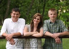 two boys and a girl are posing on a fence