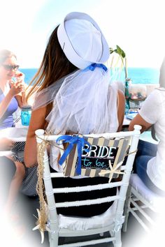 two women sitting in chairs on the beach with their backs to each other, one wearing a white hat