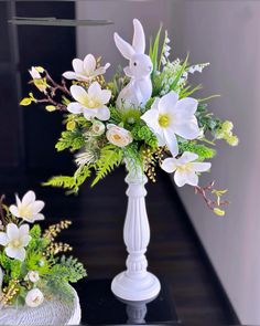 two white vases filled with flowers and greenery on a table next to each other