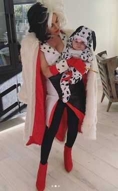 a woman holding a baby dressed in dalmatian clothing and boots, while standing on a hard wood floor