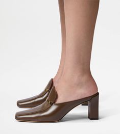 Characterized by a wraparound heel that slightly covers the heel, these mules decline Tod's style codes with refined 1970s vibes. The loafer-like upper, with minimal and sophisticated lines, is enriched with a branded metal bar. A perfect model from day to evening, designed to slim the figure with naturalness and elegance. Brown Mules, 70s Vibes, Area Codes, Perfect Model, Womens Mules, Metal Bar, Gift Boutique, Trainers Women, Blue Brown