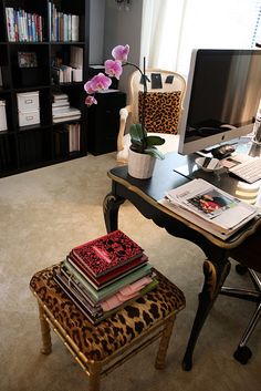 a desk with a computer on top of it next to a chair and bookshelf