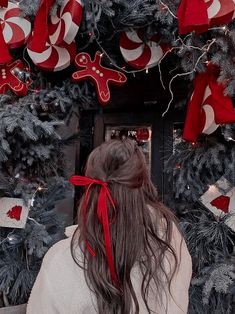 a woman with long hair standing in front of a decorated christmas tree and looking at the camera