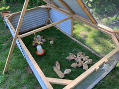 a chicken coop with chickens in the grass and an orange ball on the ground next to it