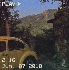 an old yellow car parked in front of a house with mountains in the background at dusk