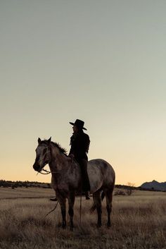 a man riding on the back of a white horse across a dry grass covered field