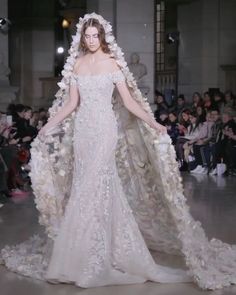 a woman in a white dress with flowers on her head and cape over her shoulders