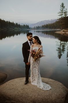 a bride and groom standing on the edge of a lake