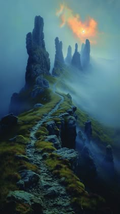 the sun is setting over some rocks on a foggy mountain side with green grass