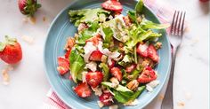 a salad with strawberries, feta cheese and walnuts on it is sitting on a white plate