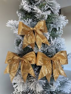 two gold bows on the top of a christmas tree with silver and white tinsel